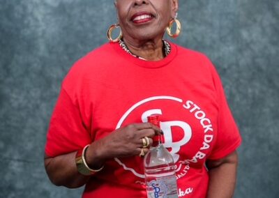 Smiling African American woman in a red t-shirt with a logo, holding a bottle of water against a blue backdrop.