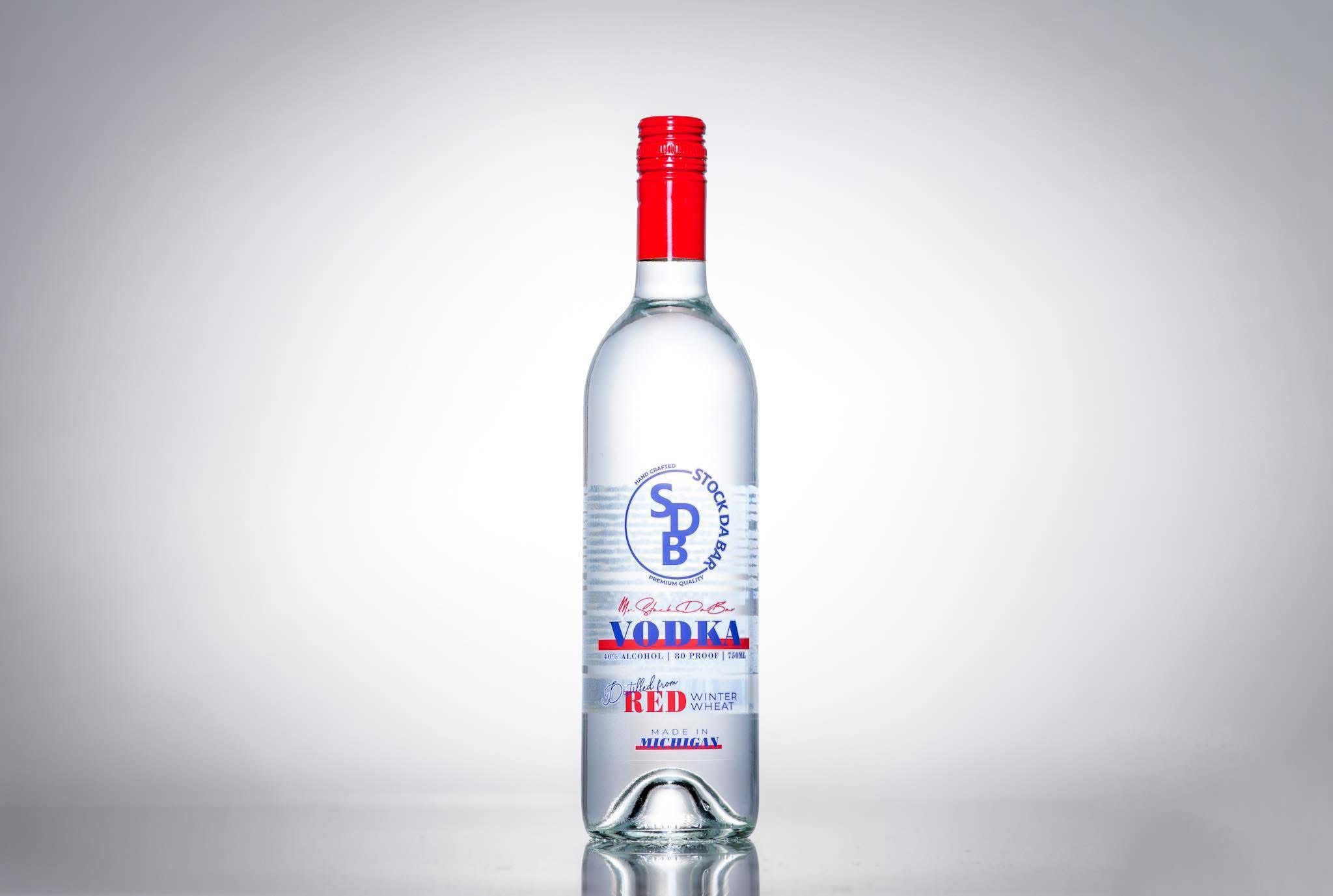 Center-aligned clear vodka bottle with a red cap, standing on a reflective surface against a gray gradient background.