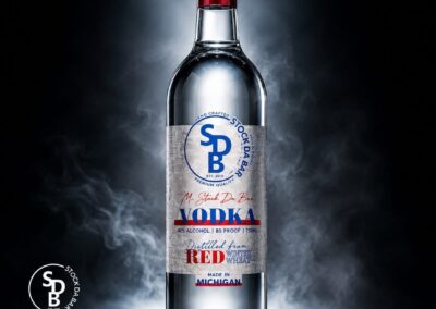 Bottle of SDV vodka with blue-red label, standing upright on a smoky dark backdrop; highlights and mist suggest premium quality.