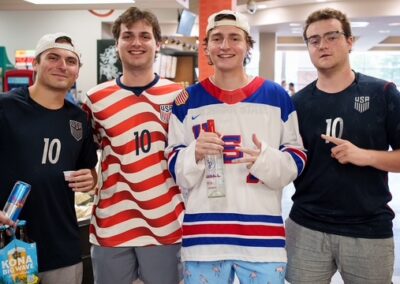 Four young men in USA hockey jerseys (numbers 10) pose and smile in a store; one holds a Red Bull, another a water bottle, and the man on the far right makes a peace sign.